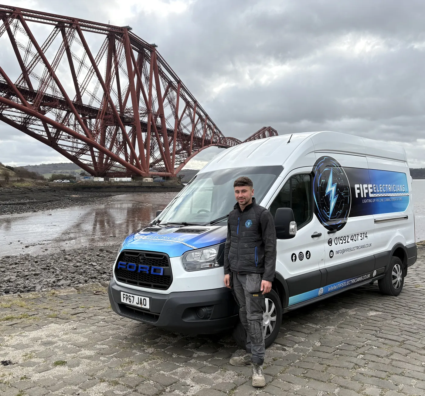 Haddon, owner of Fife Electricians, beside the company van with the Forth Bridge in the background